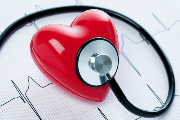 A stethoscope on a red plastic heart with EKG results in background.